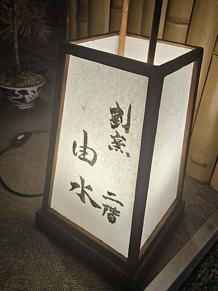 夜の竹垣の前に灯る「割烹 由水 二階」の行灯
